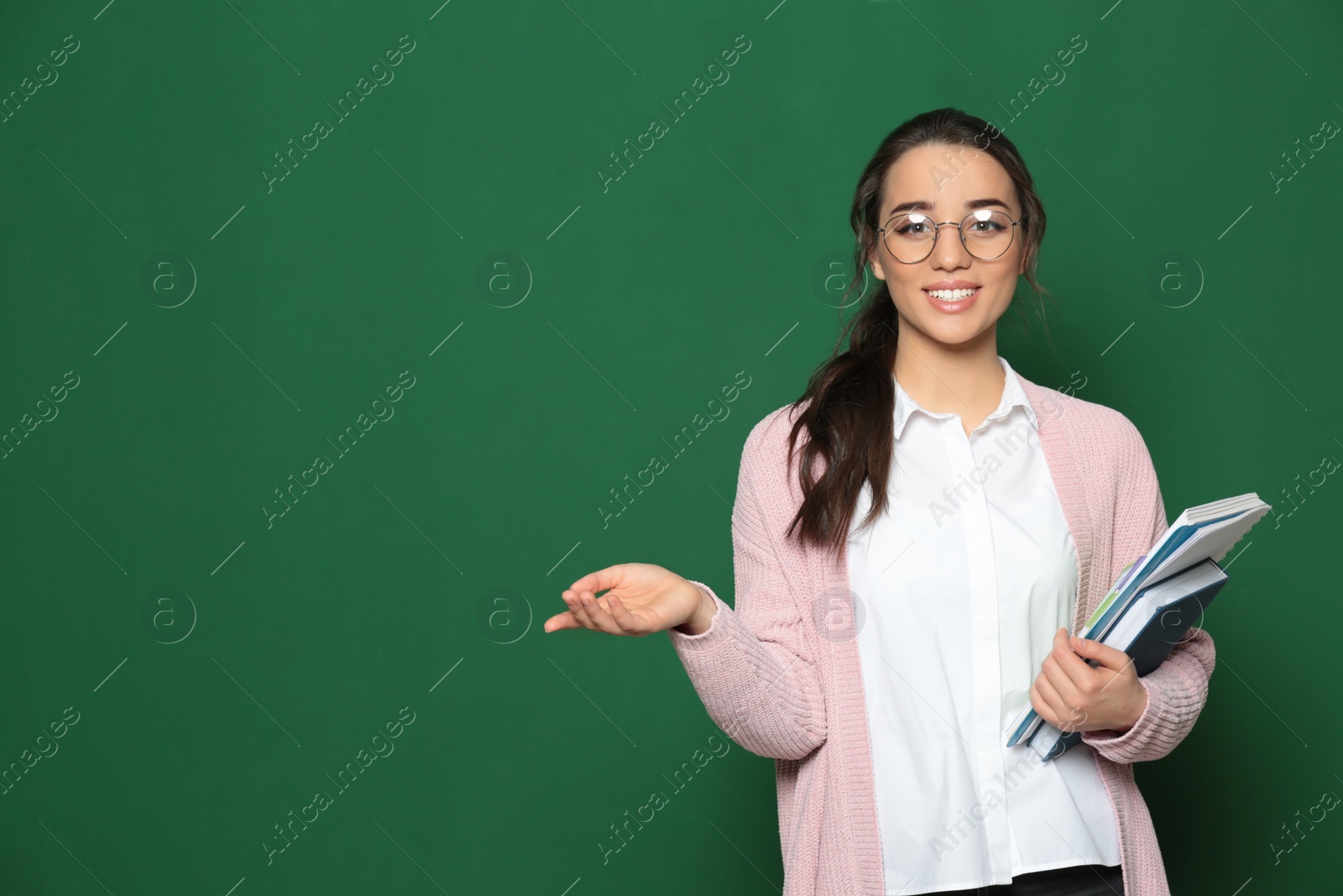 Photo of Portrait of beautiful young teacher with books near chalkboard, space for text