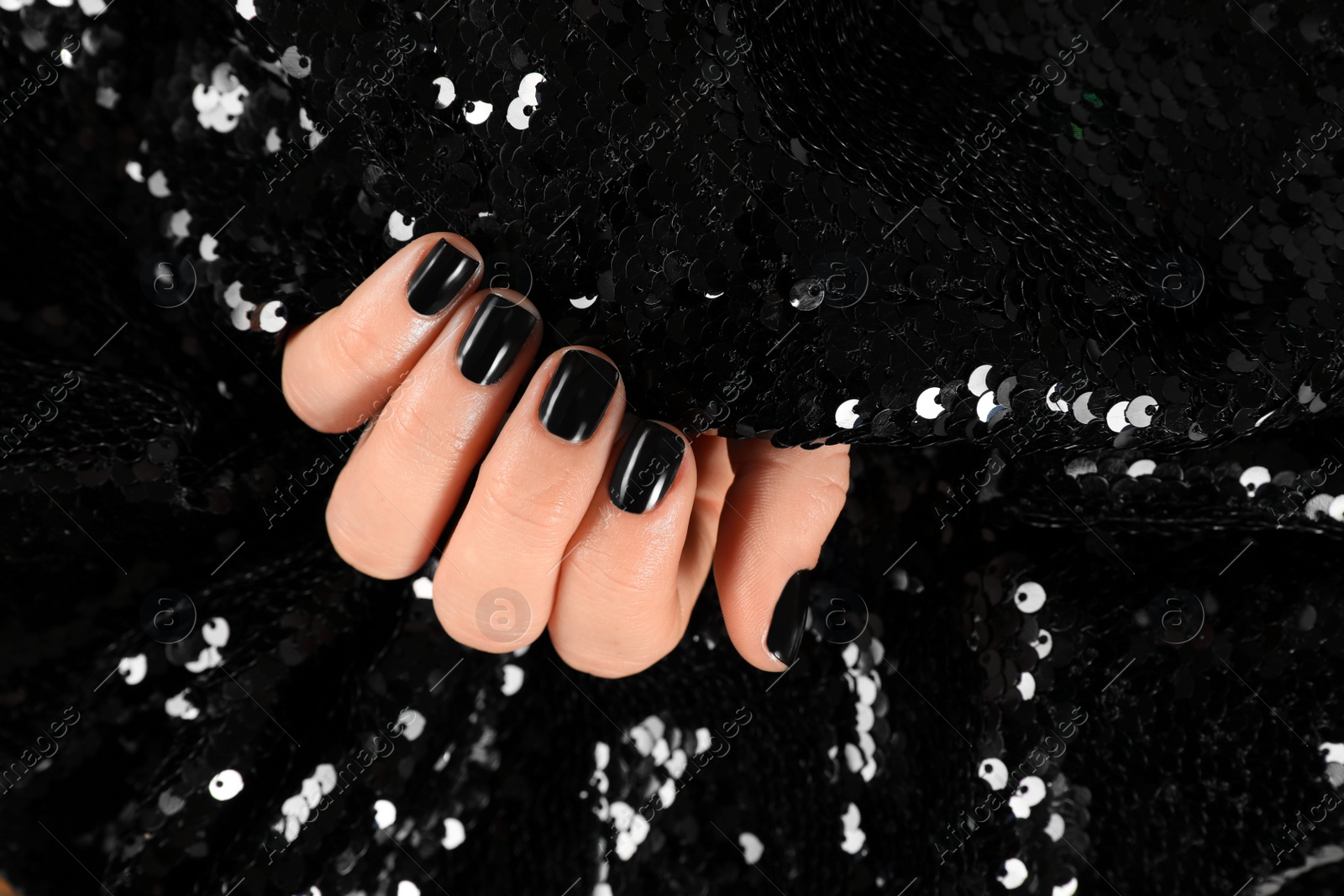 Photo of Woman with black manicure holding shiny fabric, closeup. Nail polish trends