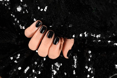 Woman with black manicure holding shiny fabric, closeup. Nail polish trends