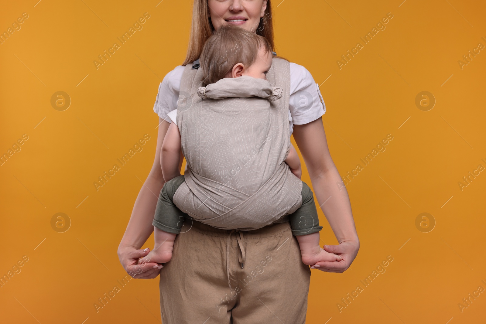 Photo of Mother holding her child in sling (baby carrier) on orange background, closeup