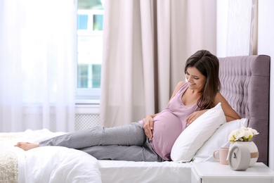 Happy pregnant woman lying on bed at home