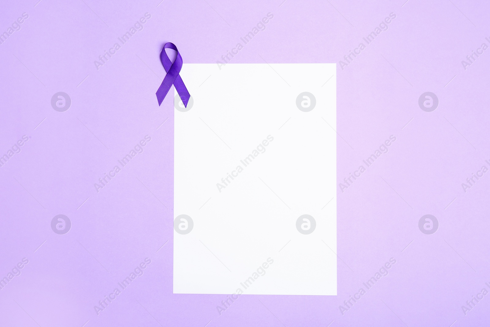 Photo of Purple awareness ribbon and blank card on lilac background, top view with space for text