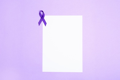 Purple awareness ribbon and blank card on lilac background, top view with space for text