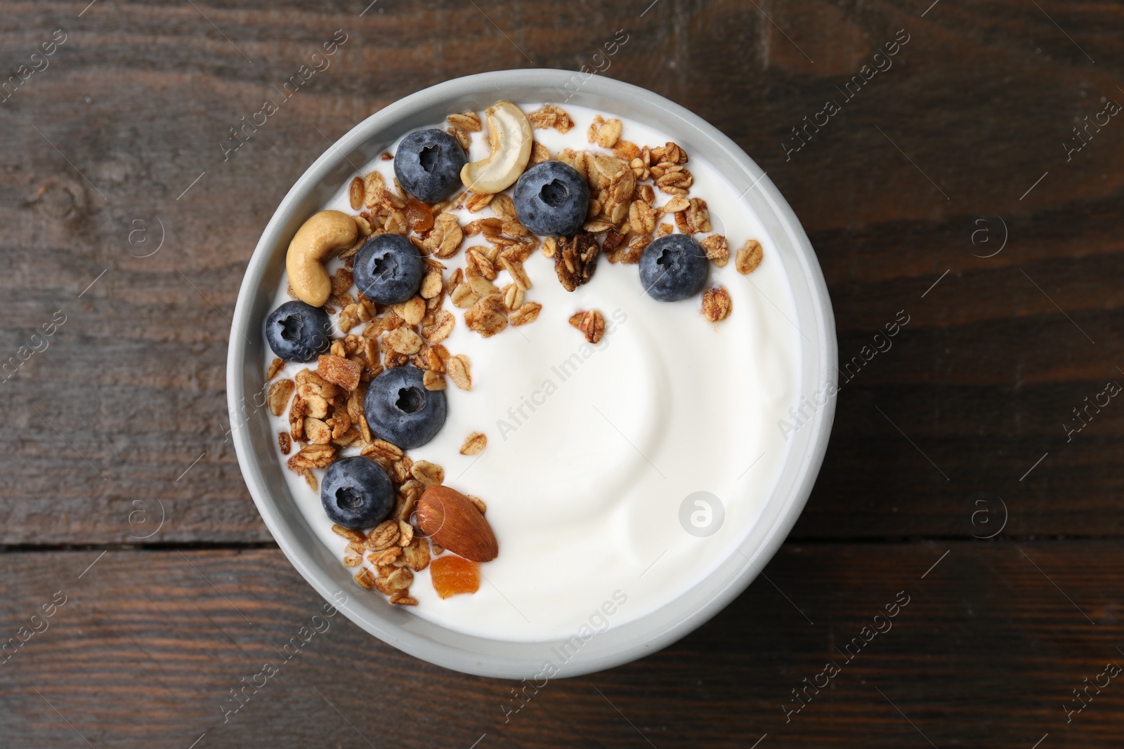 Photo of Bowl with yogurt, blueberries and granola on wooden table, top view