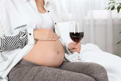 Photo of Pregnant woman with glass of red wine at home. Alcohol addiction