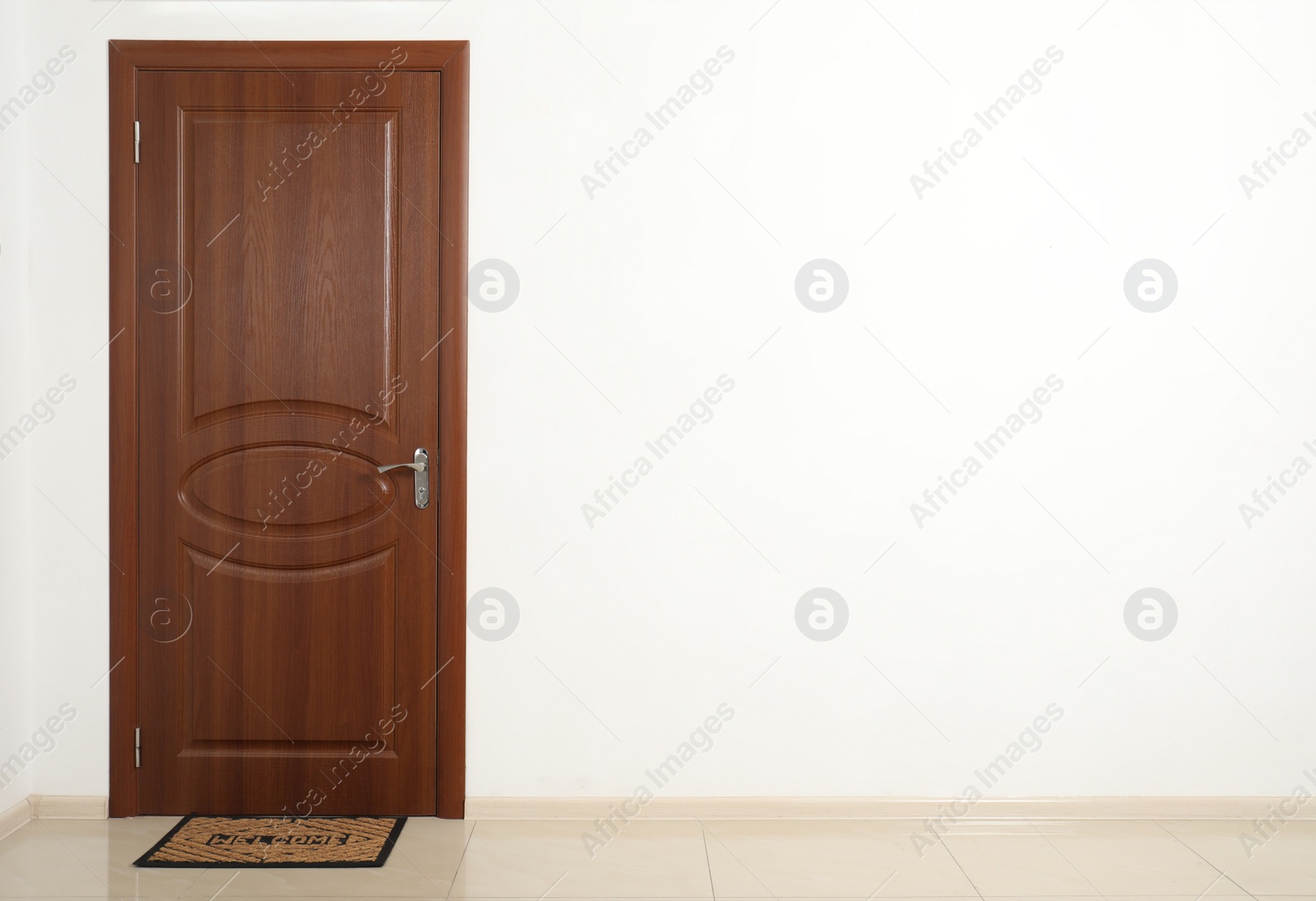 Photo of Closed brown door with welcome mat in white wall. Space for text