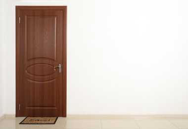 Photo of Closed brown door with welcome mat in white wall. Space for text