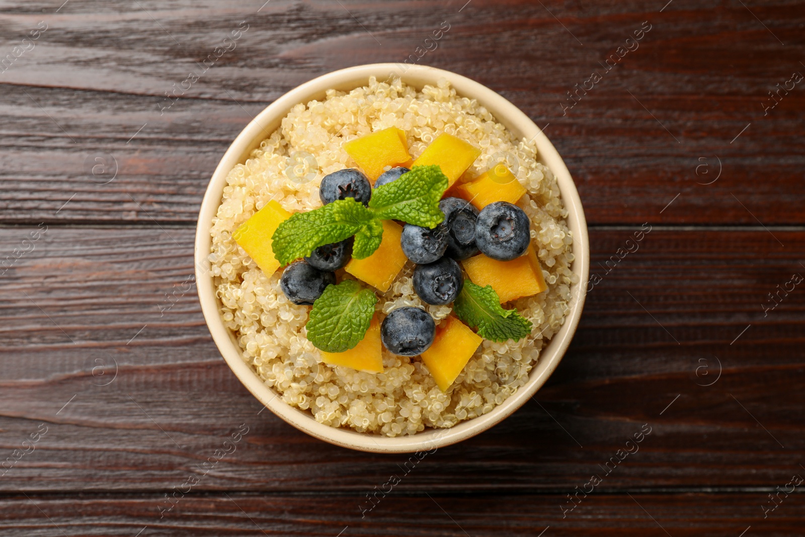 Photo of Tasty quinoa porridge with blueberries, pumpkin and mint in bowl on wooden table, top view