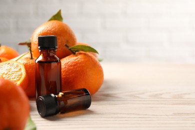 Bottles of tangerine essential oil and fresh fruits on wooden table. Space for text