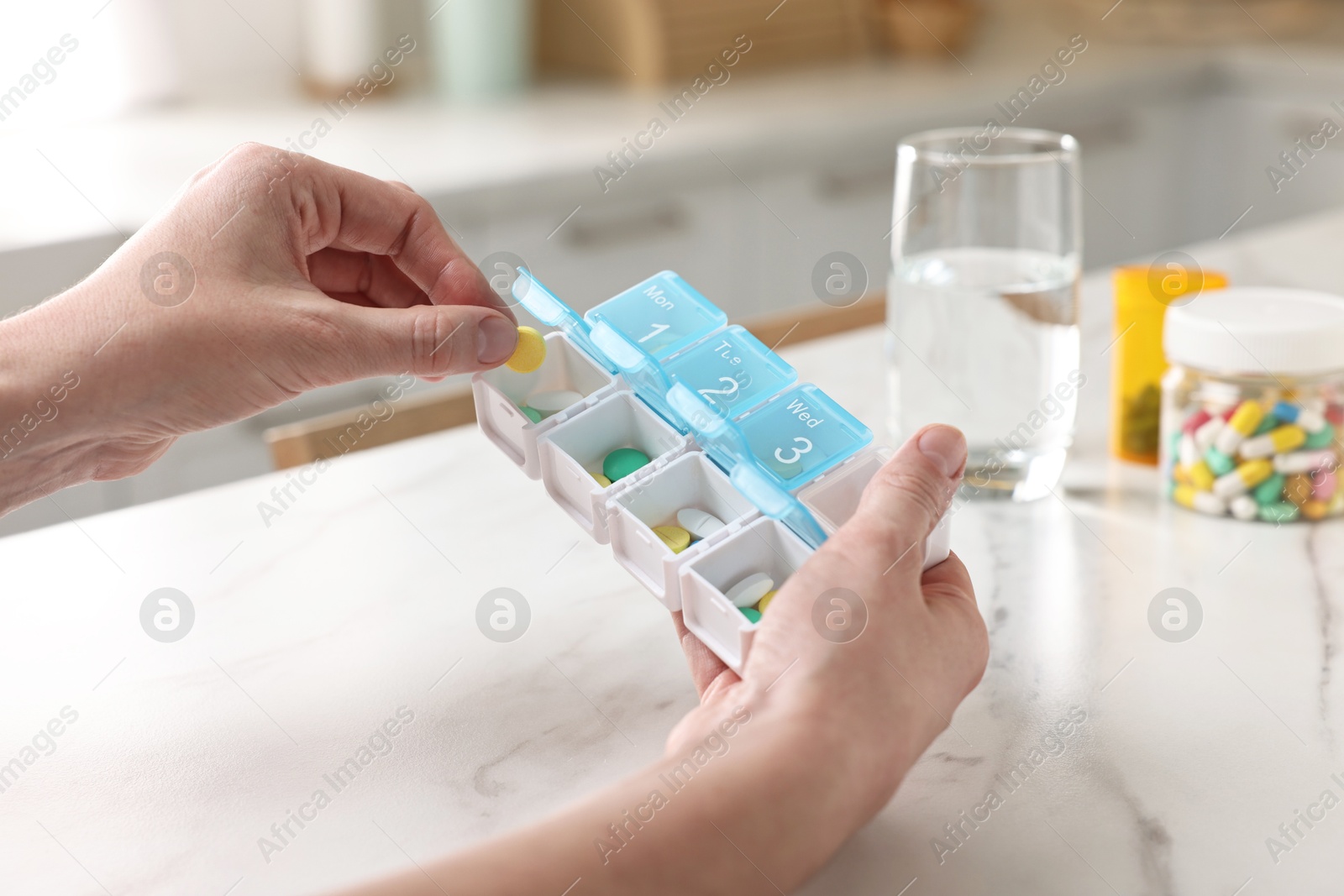 Photo of Woman with pills, organizer and glass of water at white marble table, closeup