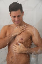 Photo of Man taking shower at home, view through glass