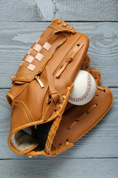 Leather baseball glove with ball on grey wooden table, top view