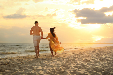 Photo of Lovely couple running together on beach at sunset, back view
