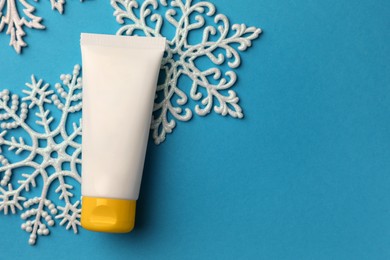 Photo of Tube of hand cream and snowflakes on light blue background, flat lay with space for text. Winter skin care