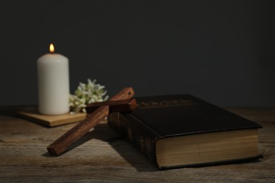 Photo of Church candle, flowers, cross and Bible on wooden table