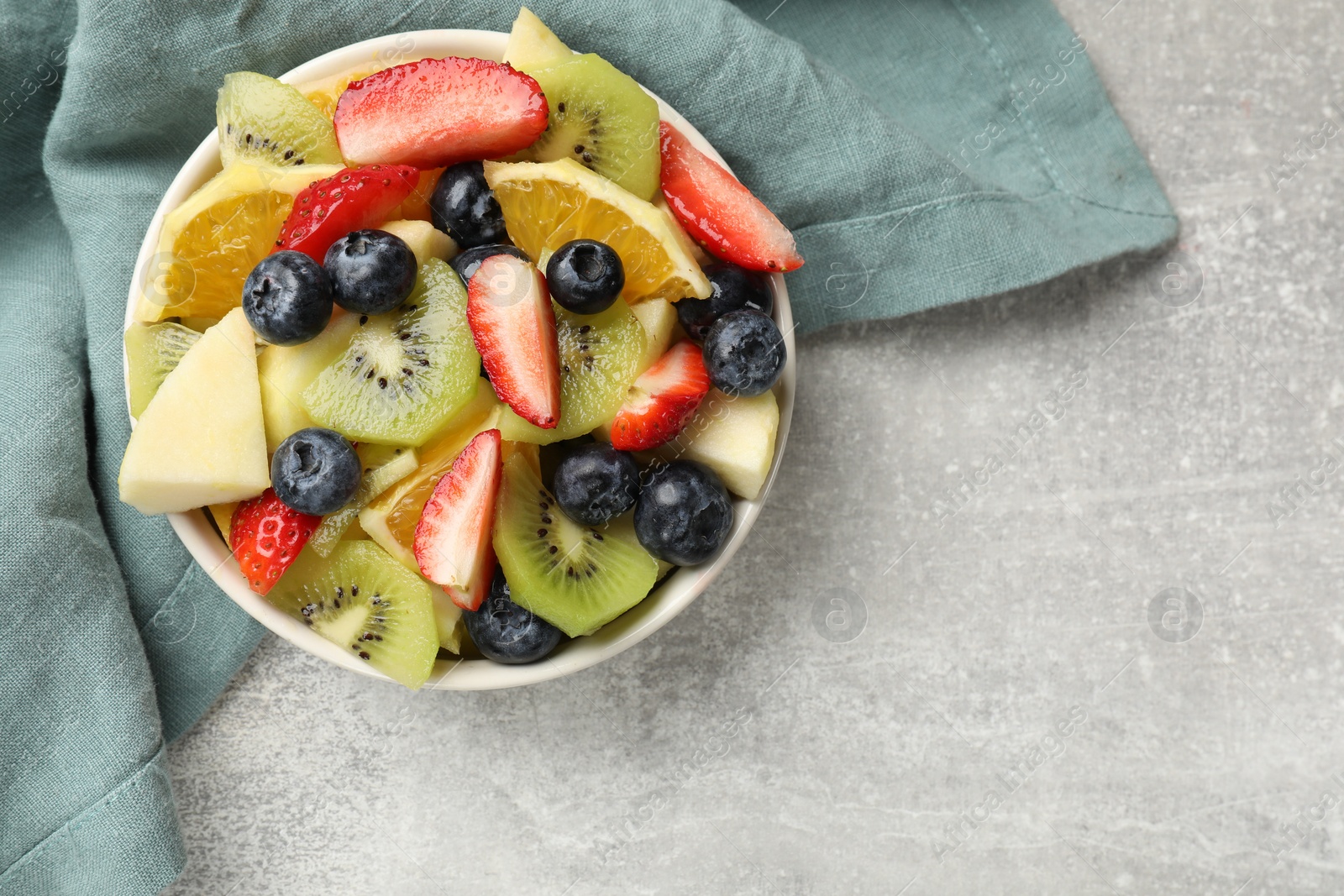 Photo of Tasty fruit salad in bowl on gray textured table, top view. Space for text