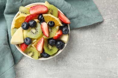 Tasty fruit salad in bowl on gray textured table, top view. Space for text