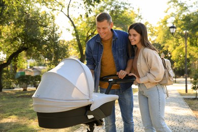 Photo of Happy parents walking with their baby in stroller at park on sunny day