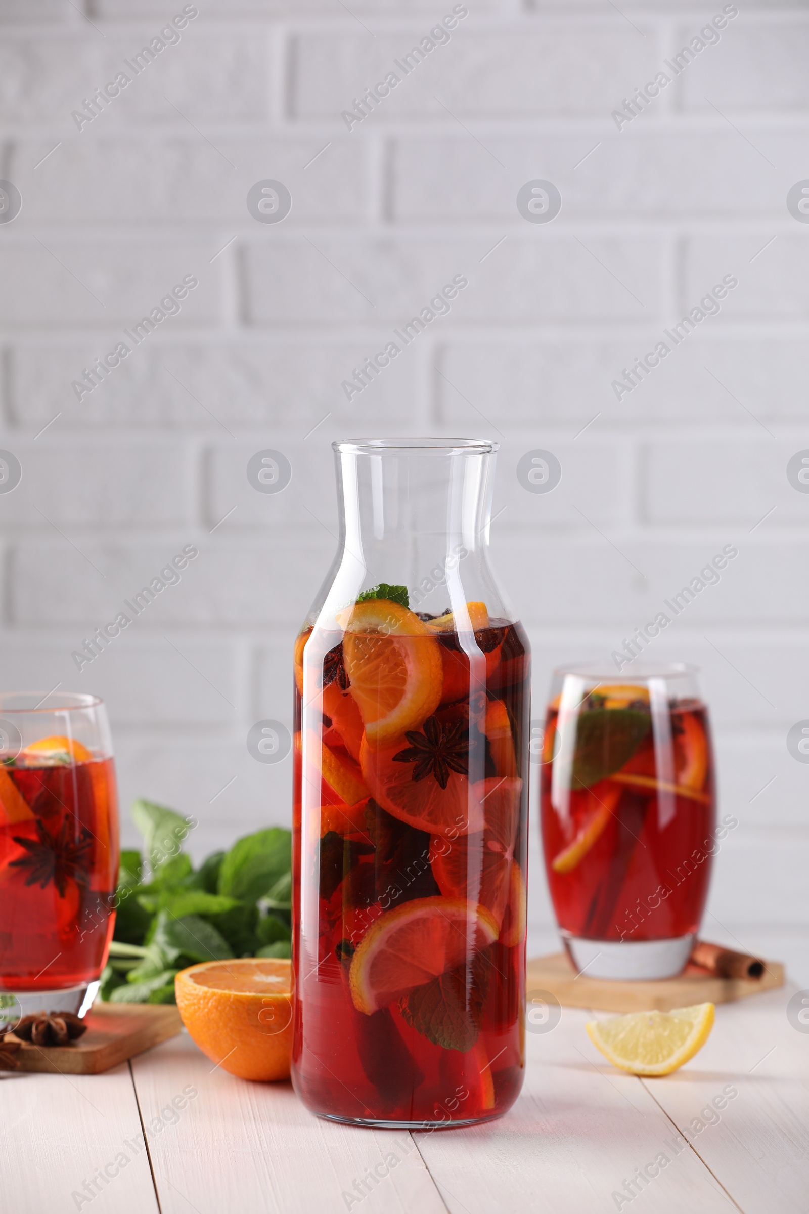 Photo of Delicious punch drink and slices of fruits on white wooden table. Space for text