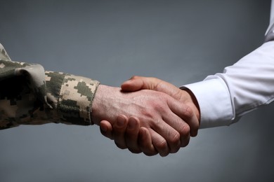 Photo of Soldier and businessman shaking hands against grey background, closeup