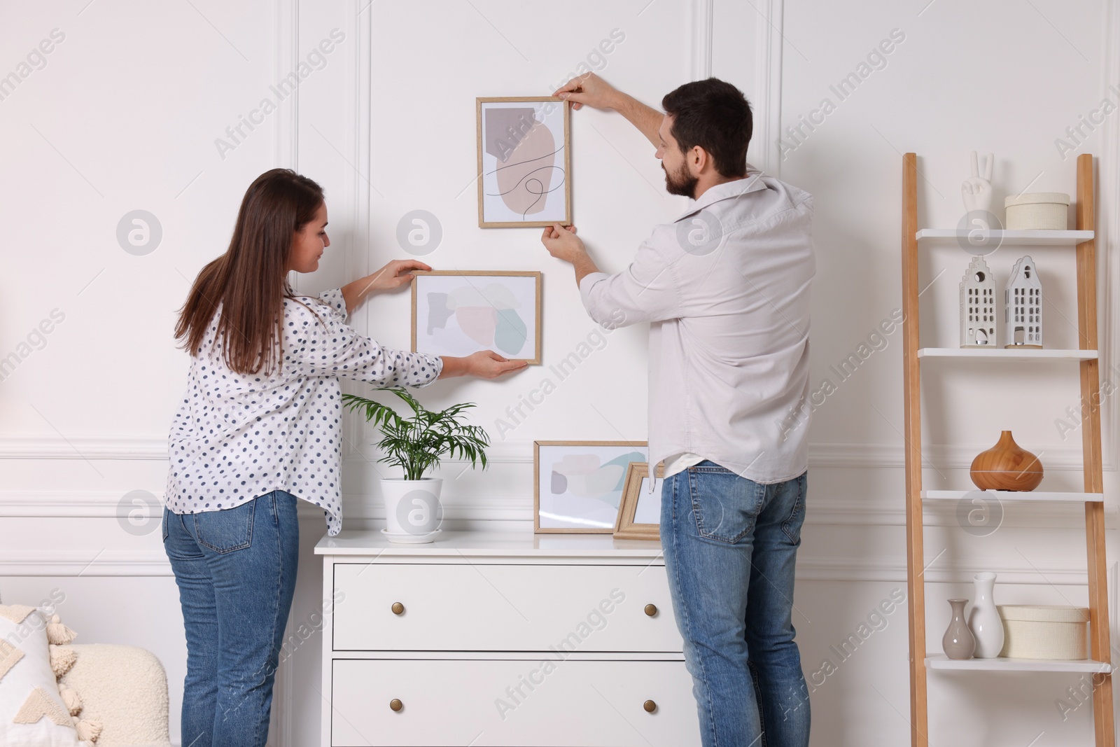 Photo of Man and woman hanging picture frames on white wall at home