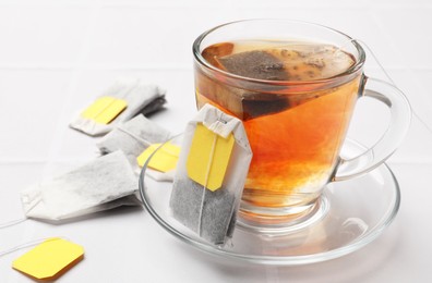 Photo of Tea bags and cup of aromatic drink on white table, closeup. Space for text