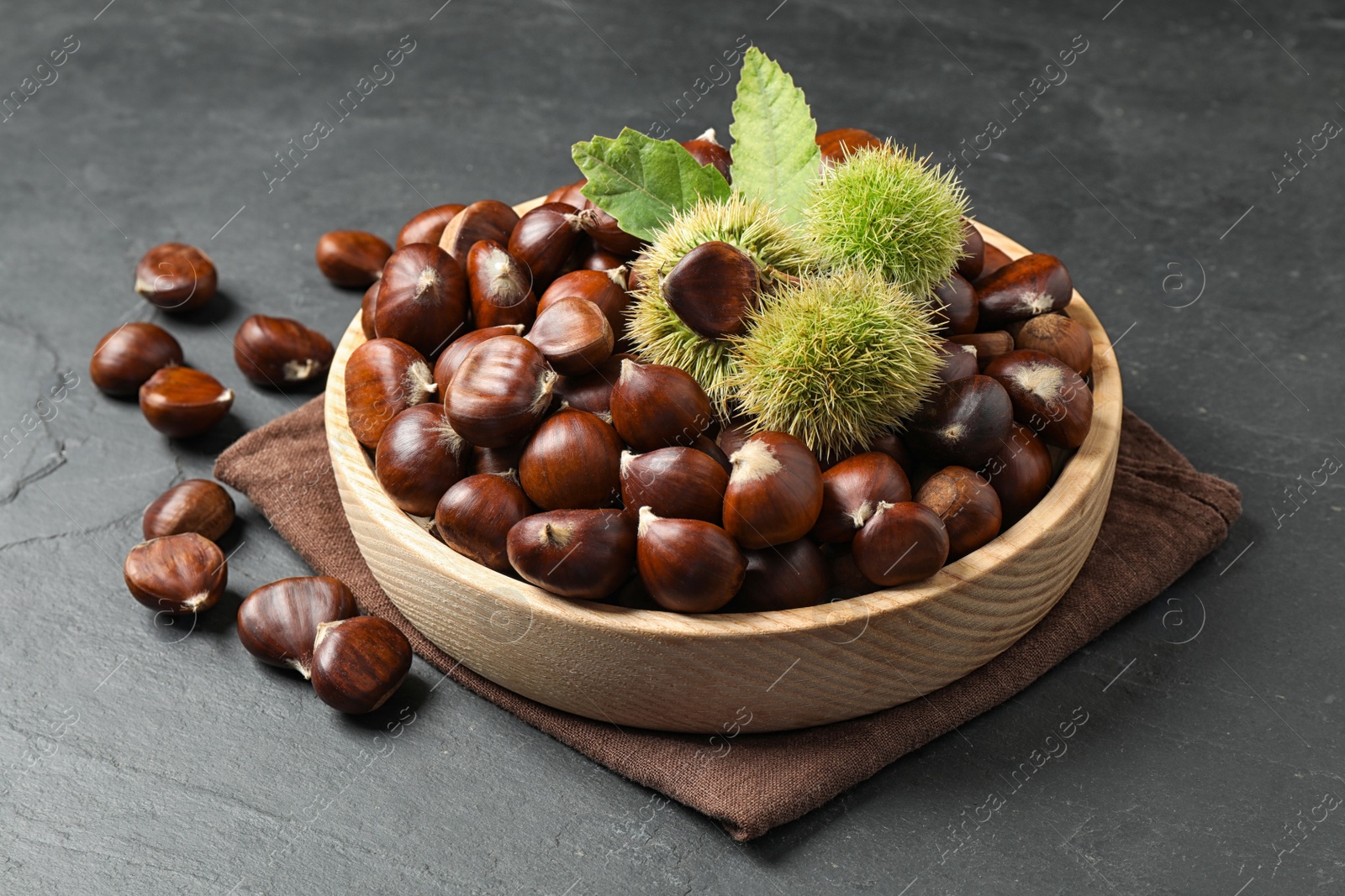 Photo of Fresh sweet edible chestnuts on black slate table