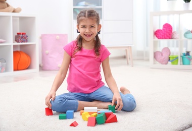 Cute child playing with colorful blocks on floor at home