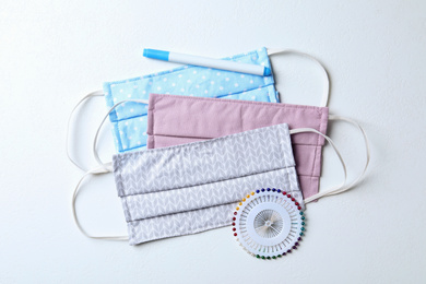 Photo of Homemade protective masks, pen and sewing pins on white background, flat lay