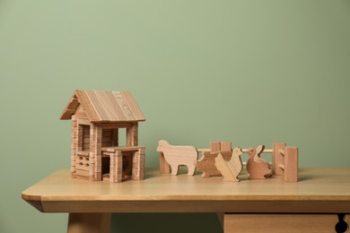 Wooden house, animals and fence on table near olive wall, space for text. Children's toys