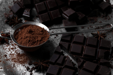 Photo of Delicious dark chocolate and cocoa powder on metal plate, closeup