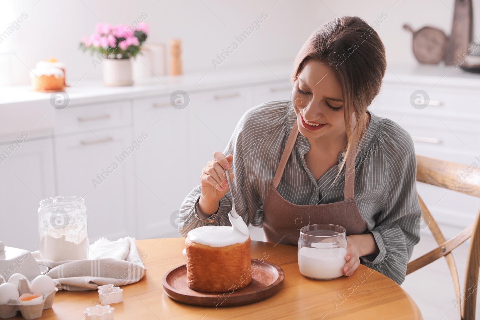 Photo of Young woman decorating traditional Easter cake with glaze in kitchen. Space for text