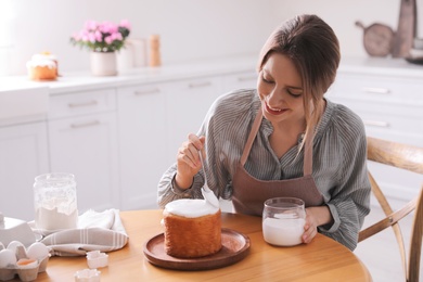 Photo of Young woman decorating traditional Easter cake with glaze in kitchen. Space for text