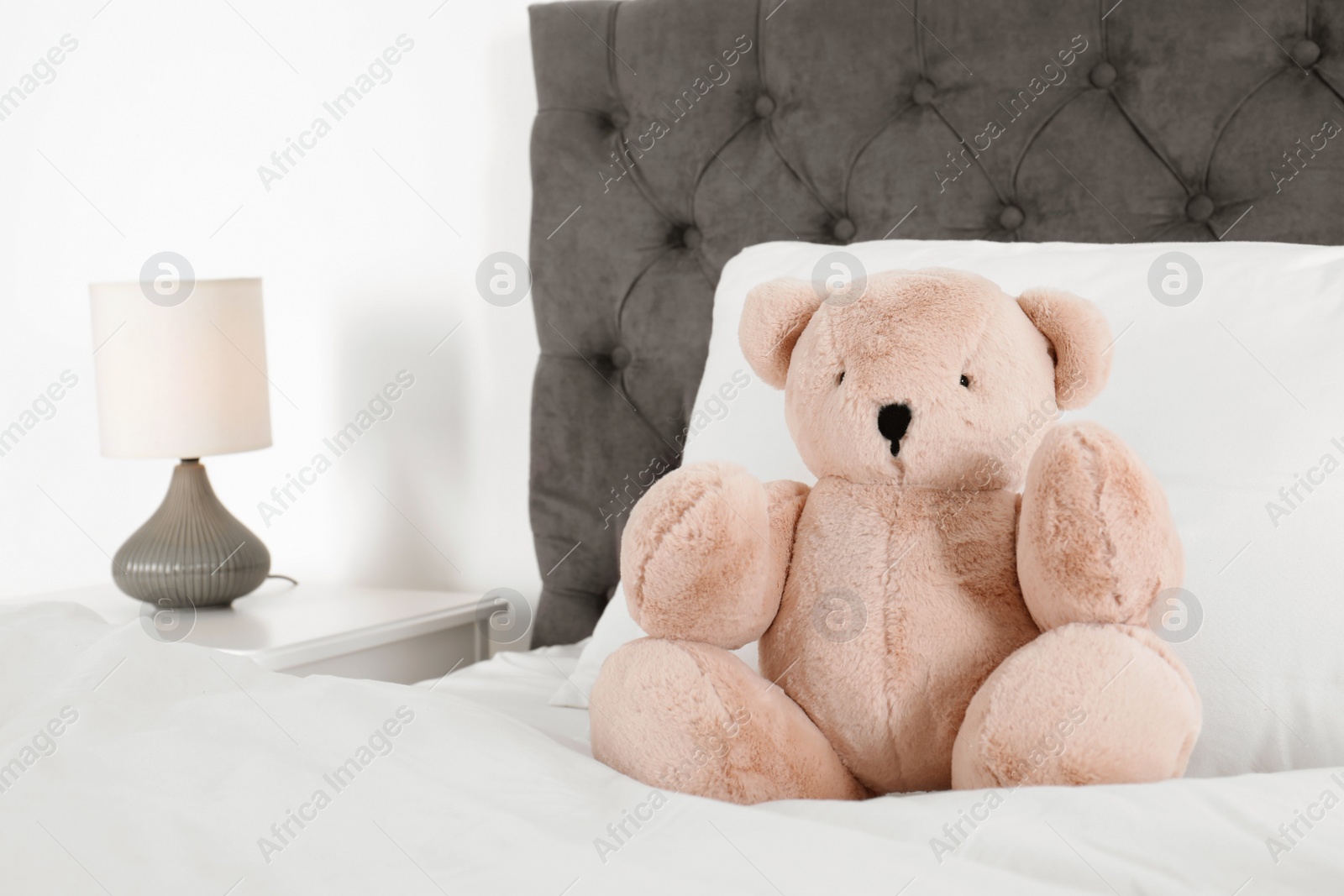 Photo of Cute teddy bear sitting on bed indoors. Space for text