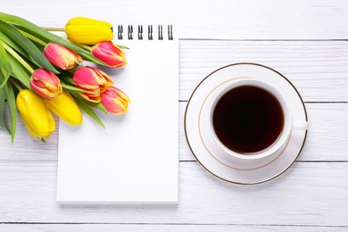Photo of Cup with coffee, bouquet of tulips and blank notebook on white wooden table, flat lay. Space for text
