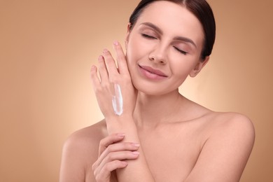 Photo of Beautiful woman with smear of body cream on her hand against light brown background. Space for text