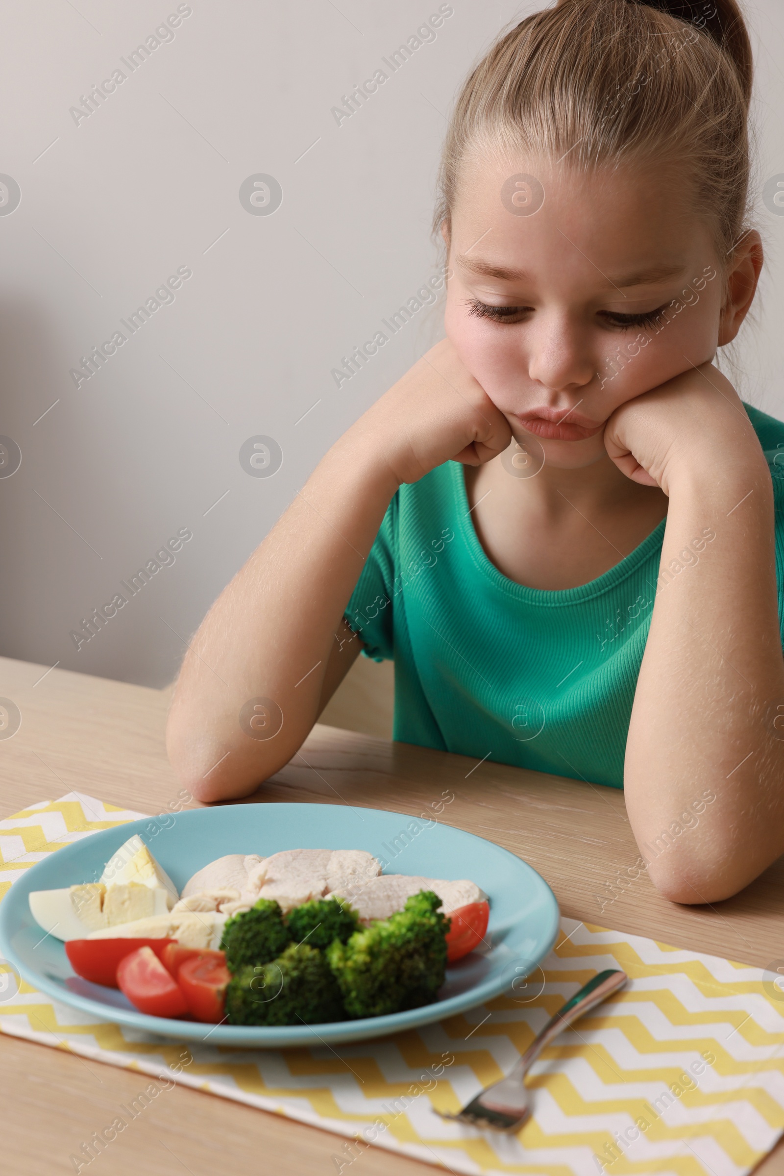 Photo of Cute little girl refusing to eat her breakfast at table on grey background