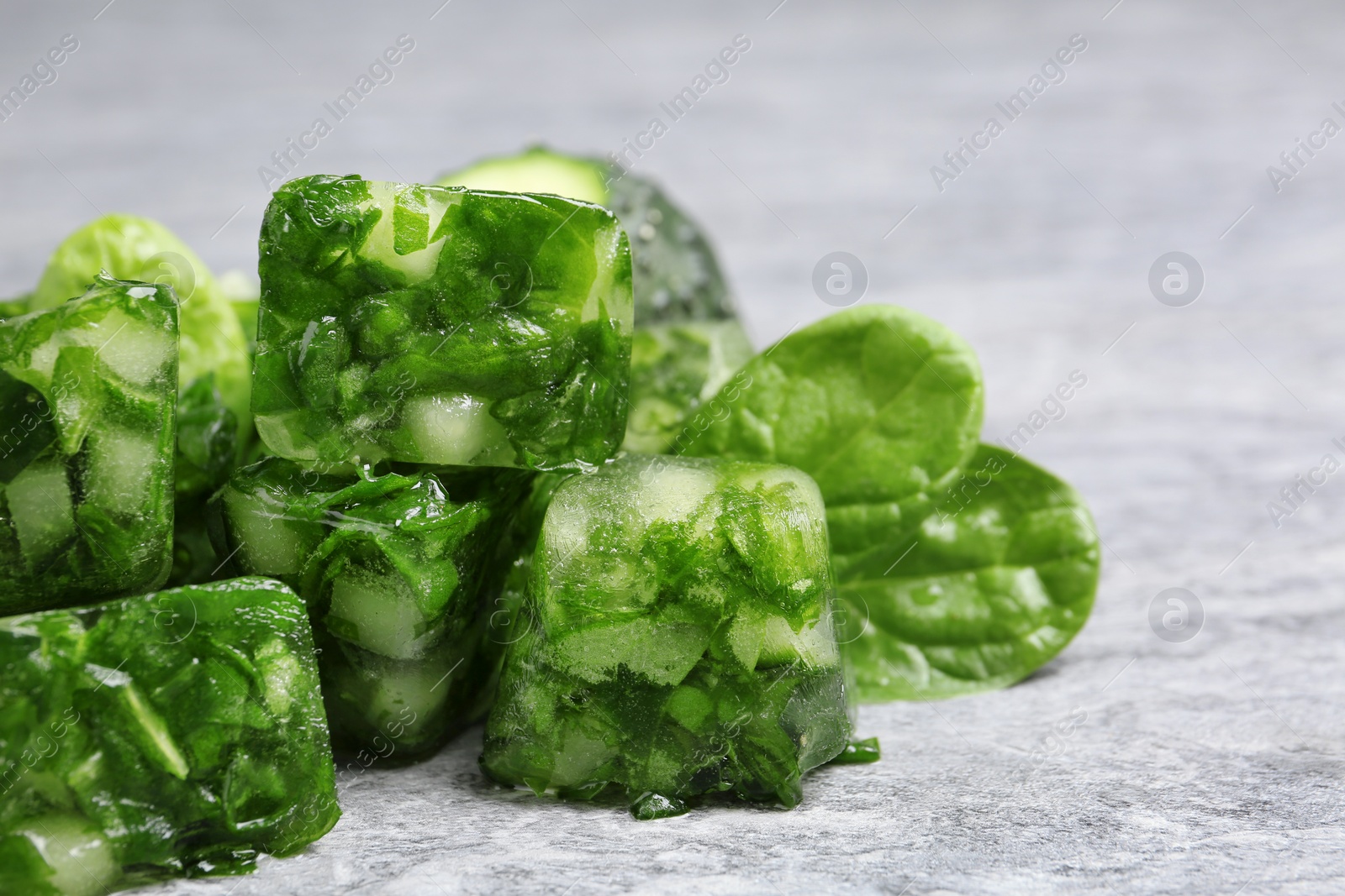 Photo of Ice cubes with cucumber slices and herbs on grey table, closeup