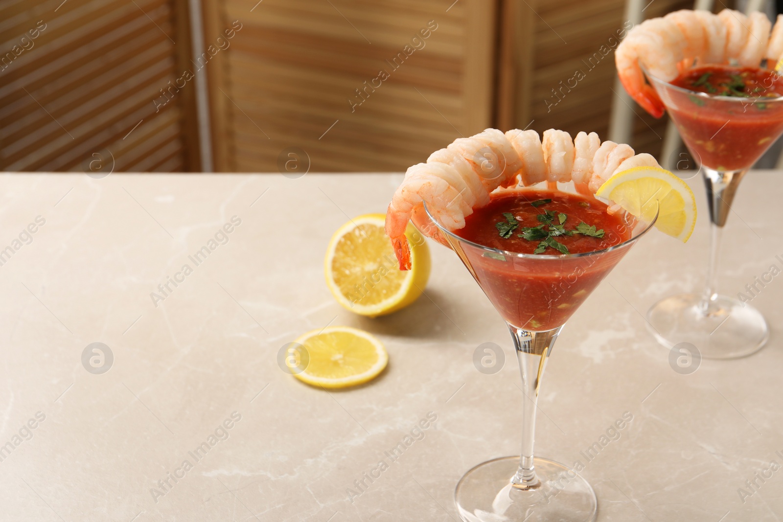 Photo of Tasty shrimp cocktail with sauce in glasses and lemon on light marble table, space for text