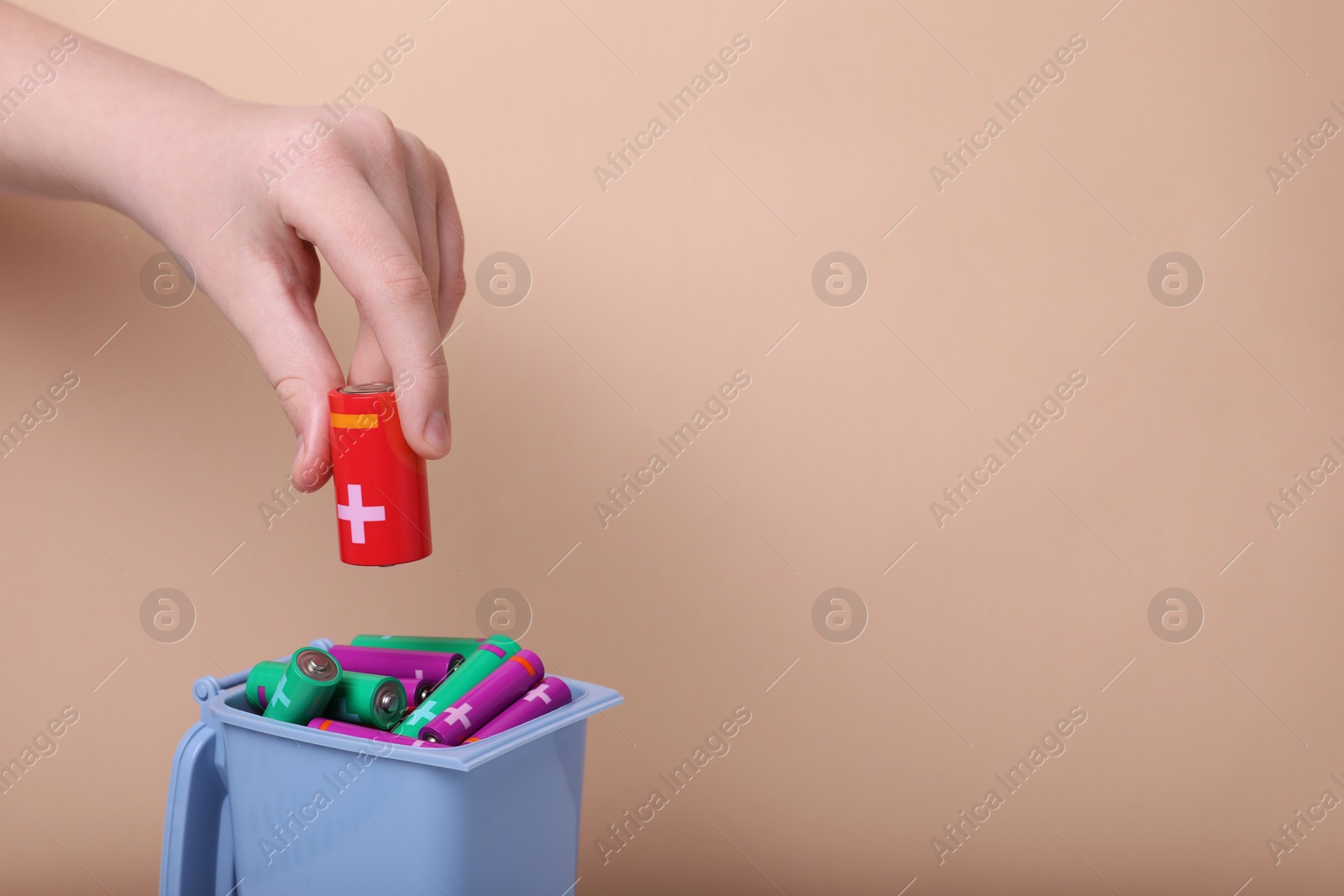Photo of Woman putting used C size battery into recycling bin on beige background, closeup. Space for text