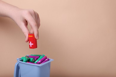 Photo of Woman putting used C size battery into recycling bin on beige background, closeup. Space for text