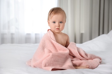Cute little baby with soft pink towel on bed after bath