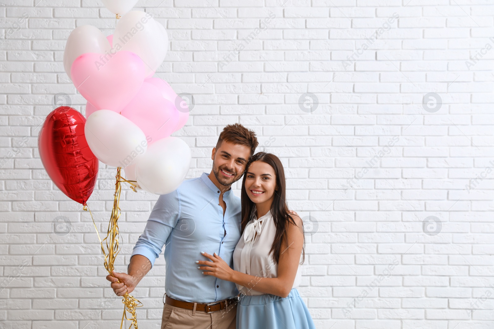 Photo of Young couple with air balloons near white brick wall. Celebration of Saint Valentine's Day