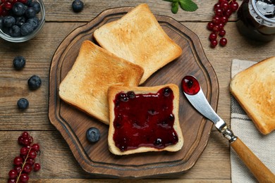 Photo of Delicious toasts served with jam and berries on wooden table, flat lay