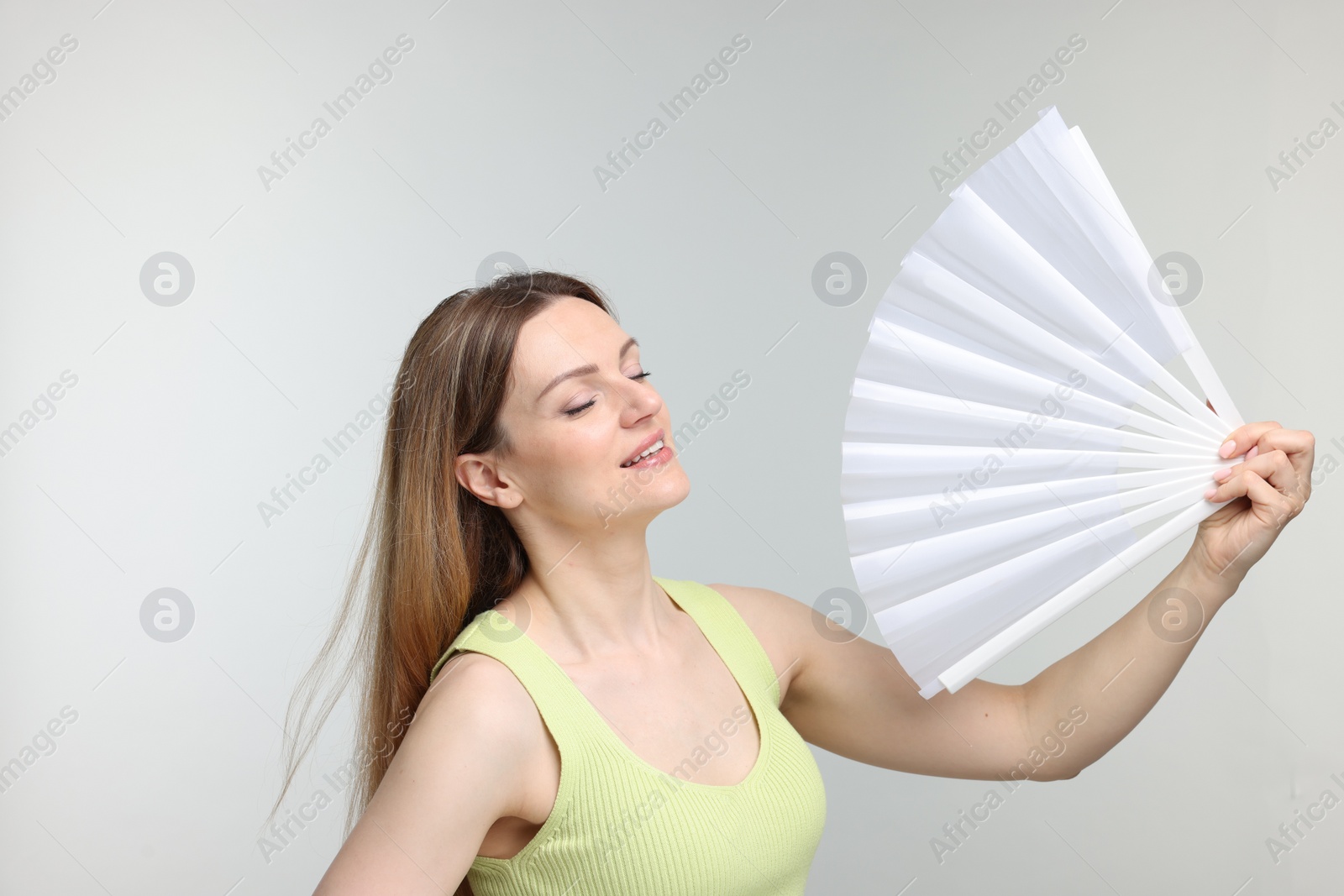 Photo of Beautiful woman waving white hand fan to cool herself on light grey background