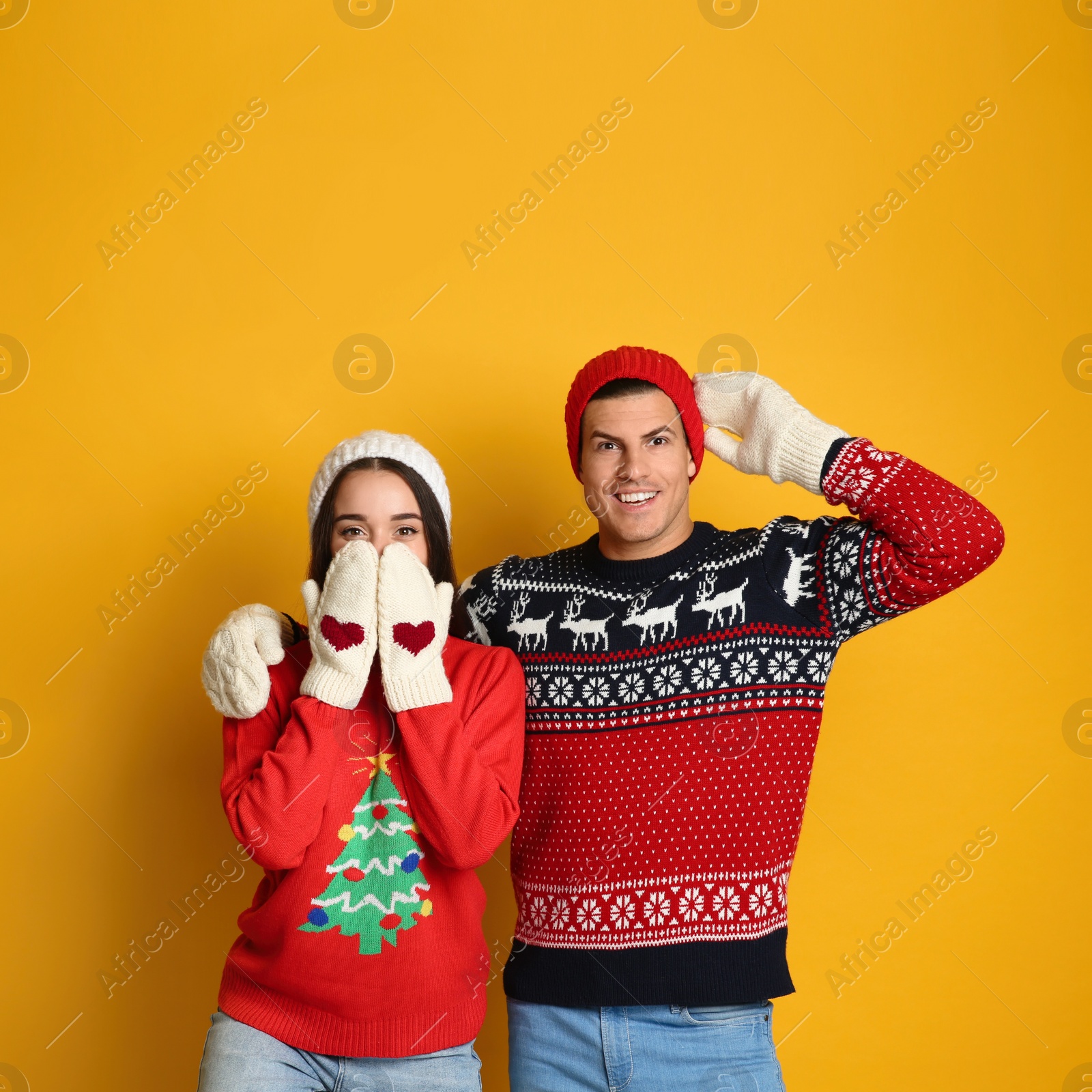 Photo of Couple in Christmas sweaters, knitted mittens and hats on yellow background