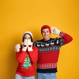 Photo of Couple in Christmas sweaters, knitted mittens and hats on yellow background