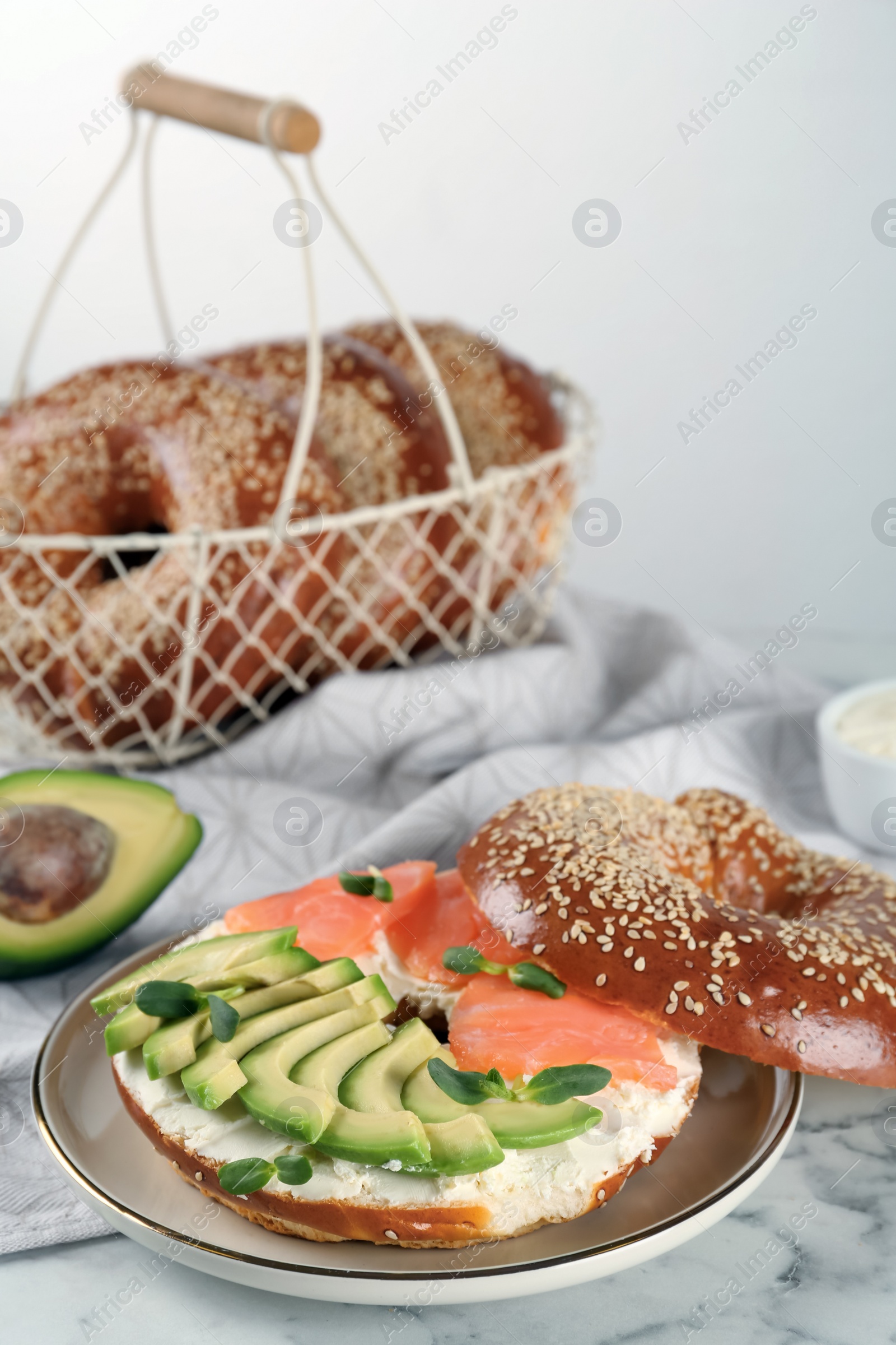 Photo of Delicious bagel with cream cheese, salmon, avocado and microgreens on white marble table