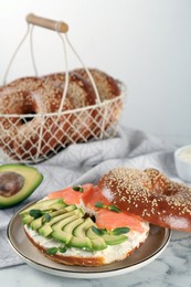 Photo of Delicious bagel with cream cheese, salmon, avocado and microgreens on white marble table