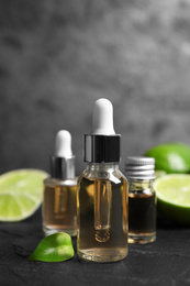 Photo of Lime essential oil and cut citrus fruits on black table